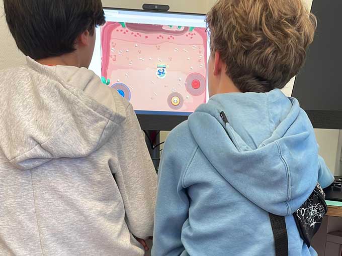Zwei Jungen von hinten sitzen vor einem Computer-Bildschirm, auf dem ein Spiel zu sehen ist
