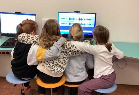 Vier Mädchen sitzen vor einem Bildschirm, auf dem Audioschnitt zu sehen ist.