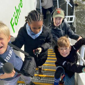 Vier Kinder gehen mit Aufnahmegerät und Mikrofon die Treppe einer Fähre hoch.